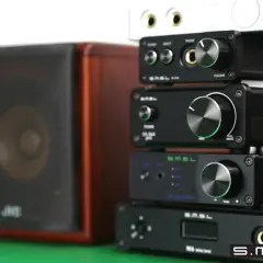 Stosik czarnych urządzeń audio SMSL, w tym SMSL M6 Mini DAC, obok brązowej kolumny głośnikowej.