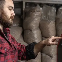 Mężczyzna w kratę reguluje panel sterowania kotła na pellet. To przykład modulacji kotła, czyli dostosowania jego pracy do potrzeb.