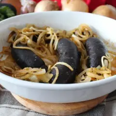 Pyszna kaszanka z piekarnika, zapieczona z cebulką w białej ceramicznej formie. Aromatyczne danie gotowe do podania.