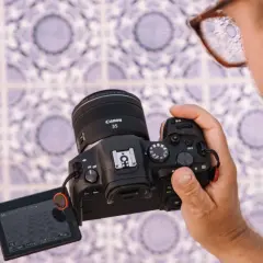 Osoba trzyma aparat Canon R6 z obiektywem 35mm, testując jego możliwości na tle wzorzystej ściany.