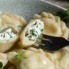 Pyszne pierogi z serem i zieloną natką, jeden uchwycony widelcem, gotowy do skosztowania.