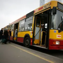 Żółto-czerwony autobus miejski z otwartymi drzwiami, pasażerowie wsiadają.