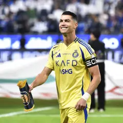 Uśmiechnięty Cristiano Ronaldo w żółtej koszulce Al Nassr, trzymający zwinięty szalik. Jego ogromne cristiano ronaldo zarobki budzą podziw.