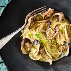 Spaghetti mit Venusmuscheln, ein köstliches Rezept. Serviert in einer schwarzen Schüssel mit einer Gabel.