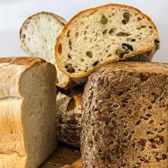Variedad de panes artesanales, incluyendo un pan blanco esponjoso, un pan con aceitunas y un pan proteico con semillas.