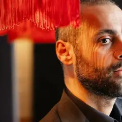 Ardalan Esmaili med ett intensivt uttryck, belyst av ett mönster av rött ljus från en lampa.