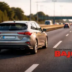 Srebrny kombi na autostradzie, gdzie obowiązują ograniczenia prędkości w Polsce. W tle inne pojazdy i logo szkoły jazdy.