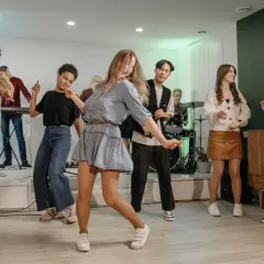 Luźne stylizacje na domówkę: jeansy, sukienki i wygodne buty. Bawiący się ludzie w różnorodnych strojach.