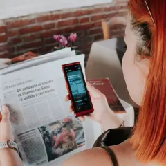Kobieta z rudymi włosami używa telefonu do tłumaczenia tekstu z gazety. To przydatna wskazówka, jak poradzić sobie na lotnisku bez znajomości języka.