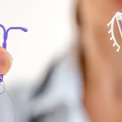 Dwie spirale domaciczne: jedna fioletowa, trzymana w palcach, druga biała z miedzianym rdzeniem.