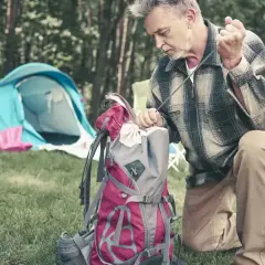Mężczyzna pakuje plecak, przygotowując się do wyprawy. W tle rozstawiony namiot. Idealny zestaw, by wiedzieć, co zabrać w góry na 5 dni.
