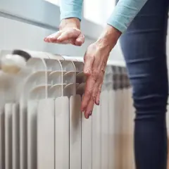 Dłonie sprawdzają temperaturę grzejnika, zastanawiając się, dlaczego grzejnik jest zimny na dole.