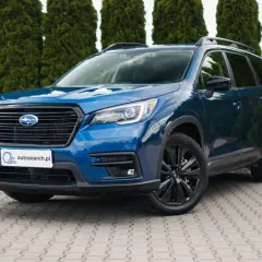 Błękitny Subaru Ascent z czarnymi felgami stoi przed żywopłotem.
