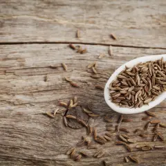 Ein Löffel voller Kreuzkümmelsamen, die für ihre verdauungsfördernde cumin wirkung bekannt sind, liegen auf rustikalem Holz.