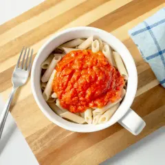 Makaron penne z sosem pomidorowym w białej misce, obok widelec i ściereczka.