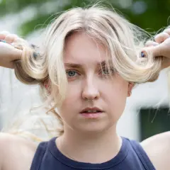 Blondes Haar, das mit Kamillentee behandelt wurde, zeigt vorher-nachher-Effekte. Die Frau hält ihre blonden Zöpfe hoch.