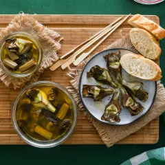 Deliciosas alcachofas confitadas en aceite de oliva, servidas con pan y palillos. Un manjar listo para disfrutar.
