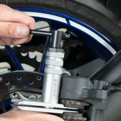 Wymiana klocków hamulcowych w motocyklu: narzędzie do cofania tłoczków zacisku hamulcowego ułatwia pracę przy tylnym kole.
