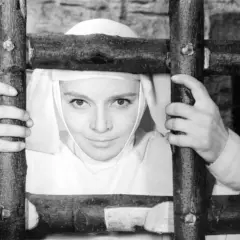 Matka Joanna od Aniołów, w białym habicie, trzyma się drewnianego krzyża. Jej oczy patrzą wprost na widza.