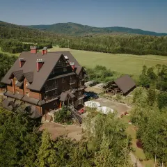 Hotel Carpatia Bieszczadzki Gościniec w otoczeniu zieleni, z drewnianym budynkiem i widokiem na góry.