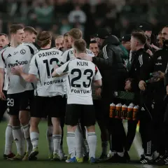 Legia Warszawa zawodnicy w białych strojach świętują na boisku. Widać numery 53, 29, 12 i 23.