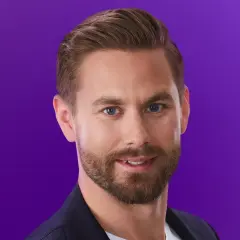 Oskar från Love is Blind, med blå ögon och skägg, ler mot kameran mot en lila bakgrund.