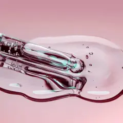 Kropla przejrzystego serum z pęcherzykami powietrza spływa z pipety na różowe tło. To fra.