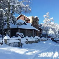 Un hermoso paisaje de Albania en invierno, con una casa cubierta de nieve y árboles nevados bajo un cielo azul brillante.