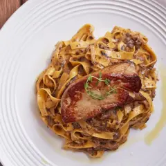 Pasta con foie gras, un plato gourmet con un trozo dorado de foie gras sobre una cama de fettuccine cremoso.