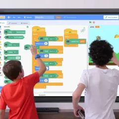 Zwei Kinder lernen Programmieren an einer digitalen Tafel in der Schule. Sie erstellen ein Spiel mit Scratch, das auf einem micro:bit basiert.