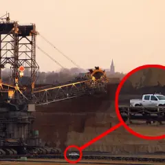 Największa koparka świata w kopalni odkrywkowej. W oddali widać mały biały pickup, który wygląda jak zabawka przy gigantycznej maszynie.