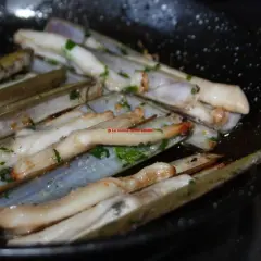 Longueirón de Fisterra cocinándose en una sartén con perejil picado. Un plato marinero listo para disfrutar.