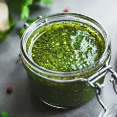 Słoik domowego pesto z bazylii, obok czosnek i świeże zioła. Idealne do makaronu.