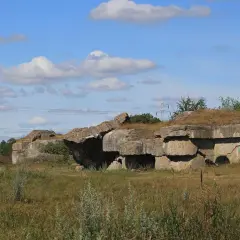 Ruiny fortu Osowiec, betonowe bunkry porośnięte trawą, na tle błękitnego nieba z chmurami.