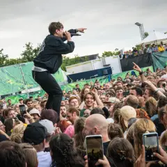 Sänger auf dem Dach eines Containers beim Green Juice Festival, der ins jubelnde Publikum zeigt. Viele Handys halten die Momente fest.