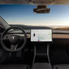 Wnętrze Tesla Model S z dużym ekranem dotykowym, kierownicą i widokiem na krajobraz za oknem.