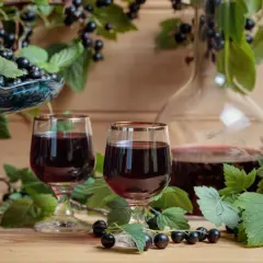 Dwa kieliszki ciemnego likieru, jakby z samego Chambord, otoczone świeżymi czarnymi porzeczkami i liśćmi.