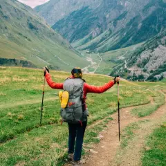 A hiker with a large backpack and trekking poles embraces the stunning alpine scenery on a self-guided tour du mont blanc.