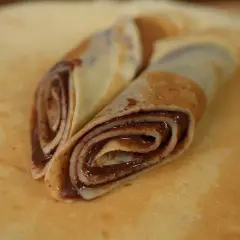 Zwei gerollte low carb pfannkuchen mit Schokoladencreme, auf einem größeren Pfannkuchen liegend.