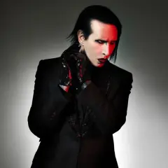 Marilyn Manson, wokalista zespołu, w czarnym garniturze i błyszczących rękawiczkach, z czerwonym światłem na twarzy.