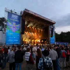 Menschenmenge vor einer Bühne beim lautfeuer festival. Scheinwerfer beleuchten die Bühne, auf der Musiker spielen.