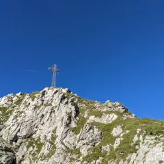 Kamienna ścieżka prowadzi pod górę, gdzie widać krzyż na szczycie. W oddali widać samolot. Kolejka na Giewont to wyzwanie dla każdego turysty.