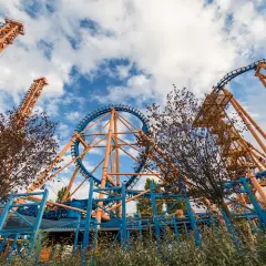 Montaña rusa naranja y azul con cielo nublado.