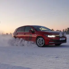 Czerwony Golf podczas kormoran snow test na zaśnieżonej drodze, z chmurą śniegu unoszącą się spod kół.