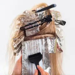 En frisör applicerar färg i slingor på blont hår, inslaget i folie. Kanske för att slinga håret gravid och känna sig extra fin.