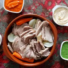 Un invitante bollito di carne, affettato e servito con carote, cipolle e tre salse: una rossa, una bianca e una verde.