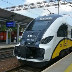 Nowoczesny pociąg KD na stacji, gotowy do odjazdu. W tle widać tablice informacyjne i fragmenty peronu.