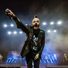 Wokalista Three Days Grace Polska z mikrofonem w dłoni, na scenie pełnej dymu i świateł.