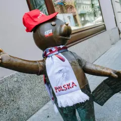 Pomnik misia z szalikiem "Polska" i czerwoną czapką, część szlaku łodzi bajkowej, pozdrawia przechodniów.