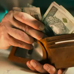 Dłonie wkładają polskie banknoty do brązowego portfela. Czy to już netto, czy jeszcze brutto?